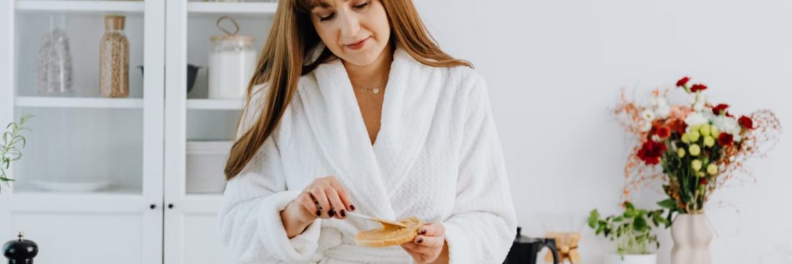 A woman in a bathrobe preparing breakfast in a home kitchen.