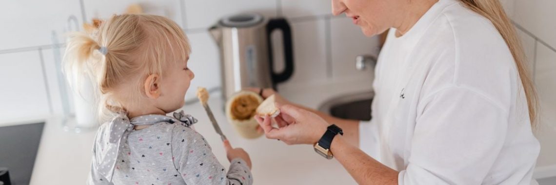 A mother and her young daughter interact while preparing food in a modern kitchen.